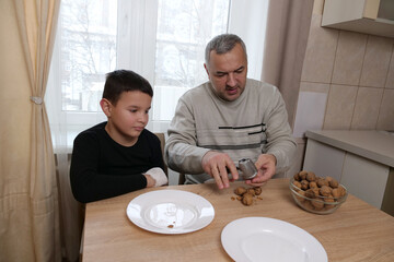 A man shows his son how to properly use a nutcracker to crack walnuts at the kitchen table.