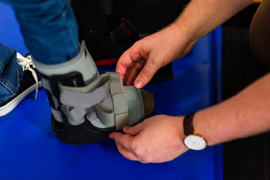 physiotherapist person strapping moon boot cast on child&rsquo;s foot after injury