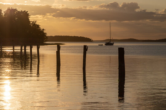 Amazing golden sunset behind the clouds during spring, over the world biggest archipelago near the city Turku seen from the village of Naantali, with calm water and a row of poles for boats to dock 