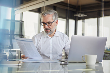 Businessman reading document at modern office desk with laptop