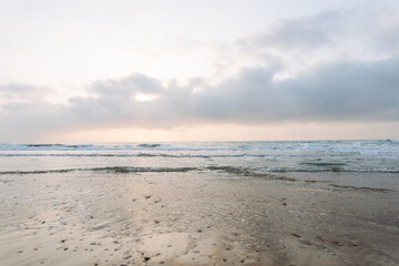 Obraz premium Seascape. Soft waves roll onto a sandy beach as the sun sets in the background. Peaceful landscape. Wildlife concept.