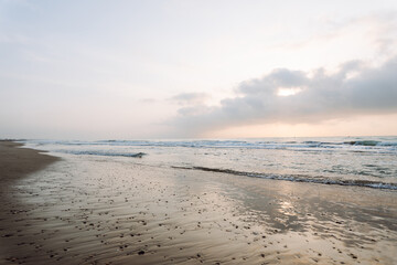 Seascape. Soft waves roll onto a sandy beach as the sun sets in the background. Peaceful landscape. Wildlife concept.