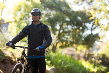 Male cyclist pausing on forest trail with mountain bike wearing helmet sunglasses hydration pack