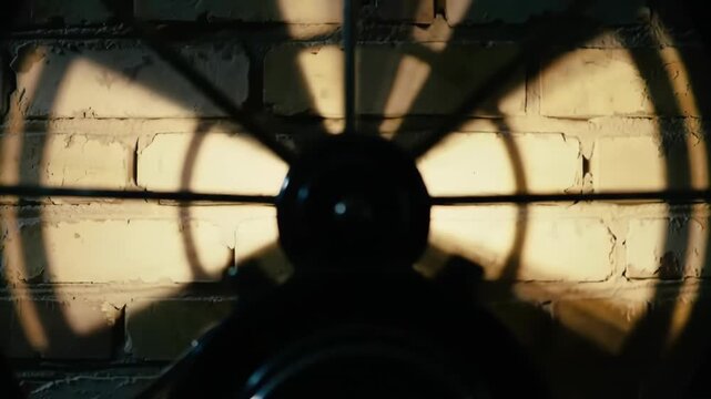 Silhouette of vintage industrial fan against brick wall casting a fan blade shadow, with dark and moody atmosphere.