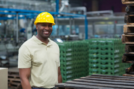 African American man standing in factory wearing yellow safety helmet beside conveyors, copy space