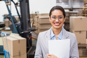 African American female warehouse supervisor holding clipboard folder in warehouse near forklift