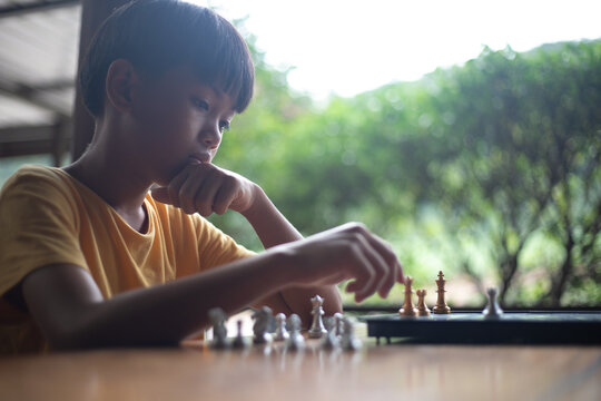 A young boy is playing chess with a thoughtful expression, hand on his chin, while planning a move. Concept of strategy, decision making, critical thinking, problem solving, childhood learning,