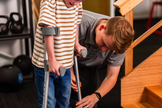Trainee physiotherapist student teaching young boy how to walk with and use crutches