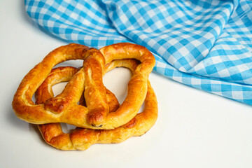 Closeup view of a pretzel loaf with a blue checkered tablecloth or napkin in a white table background. Concept of Oktoberfest. Bavarian German culture festival decoration symbol