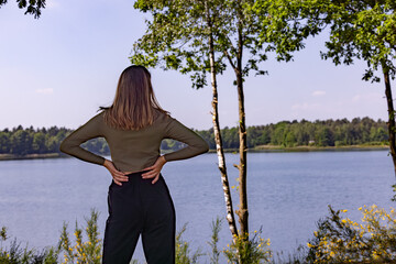 A woman stands peacefully by the serene lake, fully embracing the tranquility and inherent beauty of nature