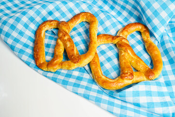 Closeup view of a pretzel loaf with a blue checkered tablecloth or napkin in a white table background. Concept of Oktoberfest. Bavarian German culture festival decoration symbol