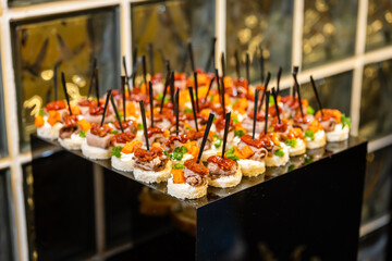 Canapes with meat and vegetables on black stand elegant appetizers at event.