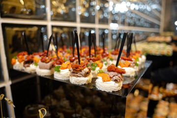 Canapes with meat and vegetables on black stand elegant appetizers at event.