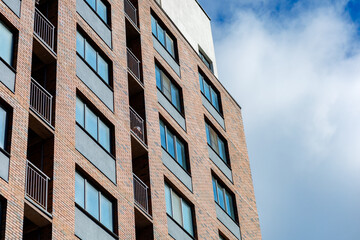 A modern apartment building with brickwork, large windows and balconies with metal railings. The facade is done in warm colors, the windows are equipped with air conditioners.