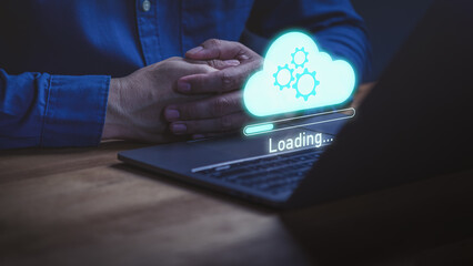 Person using laptop with a glowing holographic cloud with gears and a loading bar labeled “Loading…” represents cloud computing, data synchronization, system updates and online technology processes.