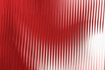 A closeup abstract view of vertical red corrugated glass with a textured surface, creating a pattern of light and shadow