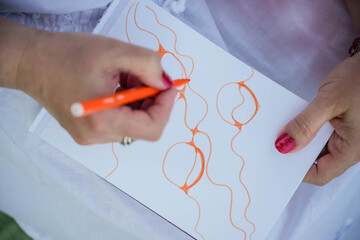 A woman draws a neurographic drawing on paper with an orange marker