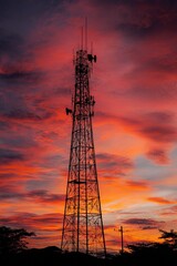 Cell tower silhouette standing tall against a fiery red orange and purple sunset sky