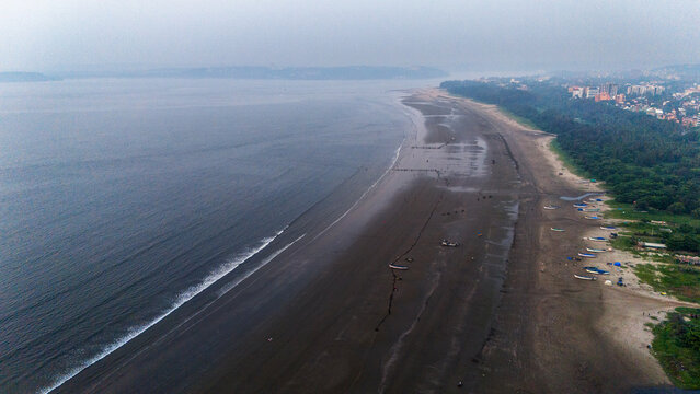 Aerial shot of Miramar Beach Goa from Dona Paula side, showcasing coastline with boats and people, Panjim city on right and vast ocean on left.