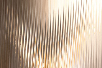 A closeup abstract view of textured glass with vertical ridges, catching warm light that creates a shimmering, rippling effect