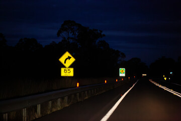 Sign on Golden Highway at night with arrow with 85 km/h recommended speed for turn