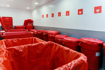 Medical waste disposal room with red biohazard containers and bins