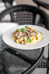 Gourmet pappardelle pasta with creamy chicken and mushroom sauce, garnished with microgreens, served on a white plate over glass table in restaurant setting