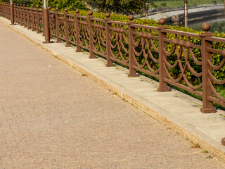 A decorative, dark brown metal railing with an intricate, repeating pattern of curved elements and...