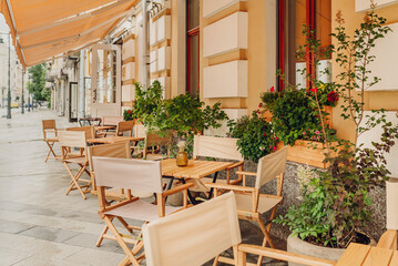 Close-up of outdoor cafe seating, featuring wooden chairs and potted plants, creating an inviting atmosphere on a rainy day