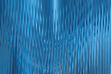 A closeup abstract view of corrugated blue metal with vertical lines and a textured, shimmering...