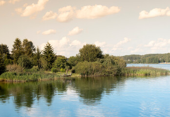 Summer river landscape with calm water. Scenic countryside view with lush grass, forest and foliage,