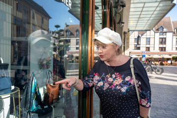 portrait d'une femme curieuse dnas la rue devant une vitrine avec des sacs