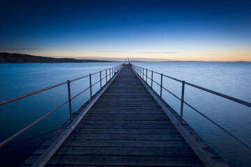 Wooden pier stretching into calm sea at dawn.