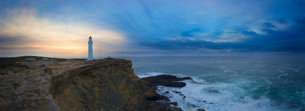 Lighthouse stands tall on a rugged coastal cliff at dusk.