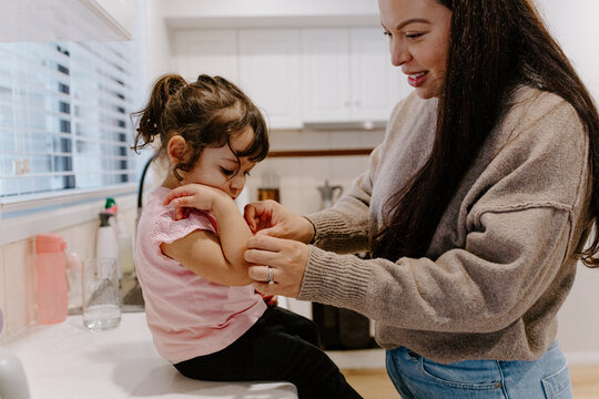 Mother applying bandaid on childs arm while seated on the kitchen counter