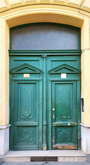 Old green wooden double door with decorative elements and weathered paint on historic building facade, vintage architecture detail