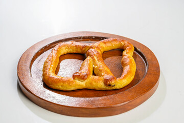 Closeup view of a pretzel loaf on a wooden tray in a white table background. Concept of Oktoberfest. Bavarian German culture festival decoration symbol