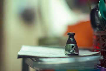 Close-up of a small metallic pressure cooker tool placed on stacked items indoors, with blurred background creating a shallow depth of field effect