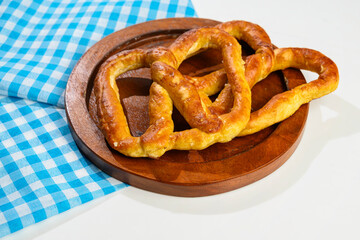 Closeup view of a pretzel loaf on a wooden tray with a blue checkered tablecloth or napkin in a white table background. Concept of Oktoberfest. Bavarian German culture festival decoration symbol