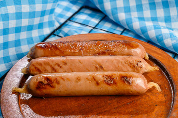 Sausage on a wooden tray with a blue checkered tablecloth or napkin background. Concept of Oktoberfest. Bavarian German culture festival decoration symbol