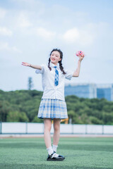 Happy teen girl in school uniform poses with a camera outdoors.