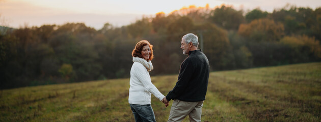 Senior couple walking hand by hand in autumn sunset light.