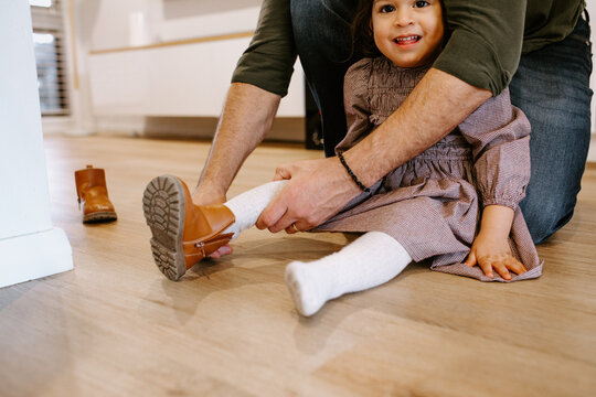 Father helping daughter put on shoes while seated on the floor