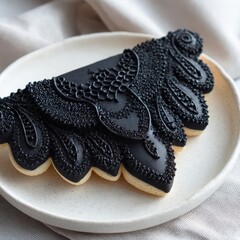 Ornate Black Iced Cookie on White Plate with Fabric Backdrop