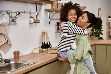 Joyful moments between African American mother and daughter in their cozy home kitchen