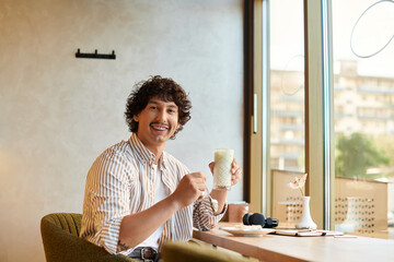 Handsome young man enjoys a refreshing drink in a cozy indoor cafe setting