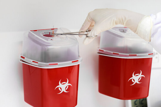 Safe disposal of medical needle in red biohazard sharps container