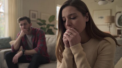 Upset woman sitting on a couch with her partner in the background during a difficult conversation at home. - Powered by Adobe