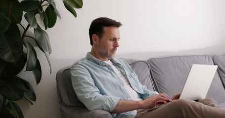 Video of mid adult man using laptop sitting on sofa - Powered by Adobe