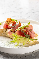 Gourmet appetizer with deli meat, frisée lettuce, red pepper, and mousse on a white plate. Minimalist fine dining presentation on stone background. Horizontal composition